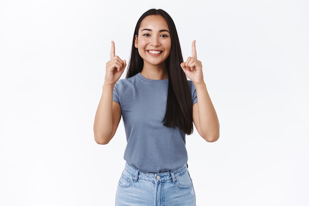 Portret van een tevreden knappe enthousiaste aziatische vrouw in t-shirt, handen opstekend en vingers omhoog om klanten te promoten en aan te moedigen, stop door op de link te klikken, volg haar pagina, glimlachend