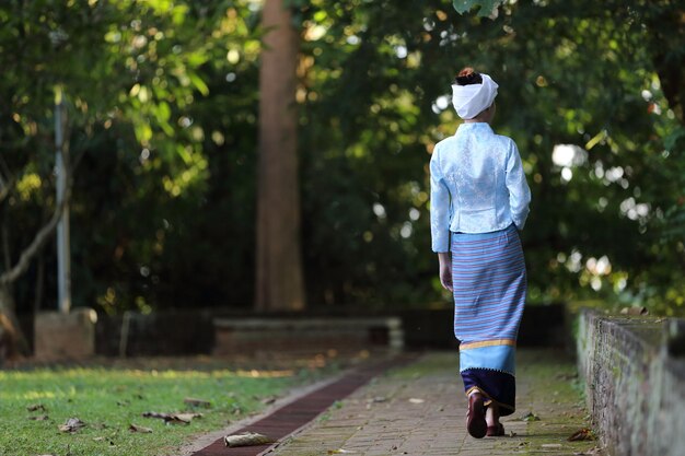 Portret van een thaise jonge vrouw met traditionele thaise kleding die in de thaise tempel loopt met boom en zonsopgang