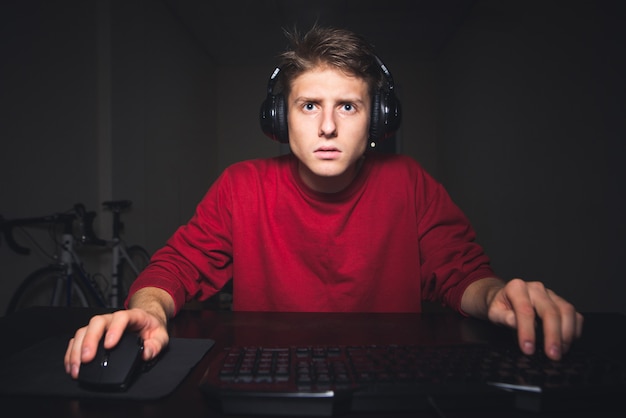 Portret van een tiener gamer zitten aan de tafel en het spelen van videogames op de computer