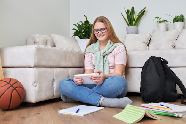 Portret van een tienermeisje dat thuis op de vloer zit met schoolboeken digitale tablet