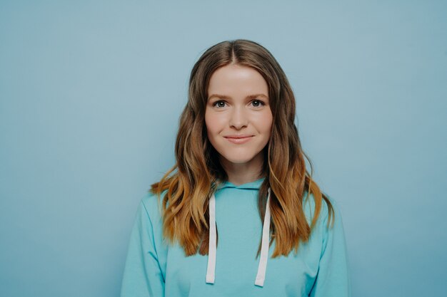 Portret van een tienermeisje met golvend ombre kapsel dat lacht terwijl ze naar de camera kijkt in een comfortabel, casual blauw sweatshirt dat tegen de achtergrond van de studio staat