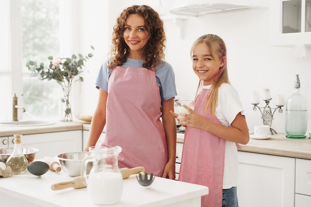 Portret van een tienermeisje met haar moeder thuis in de keuken