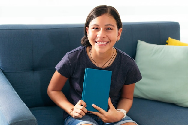 Portret van een tienermeisje zittend op de bank glimlachend kijkend naar de camera, afstandsonderwijs