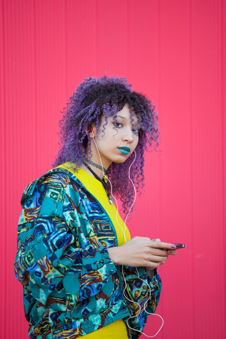 Portret van een tienervrouw die aan muziek van haar telefoon op een roze muur luistert