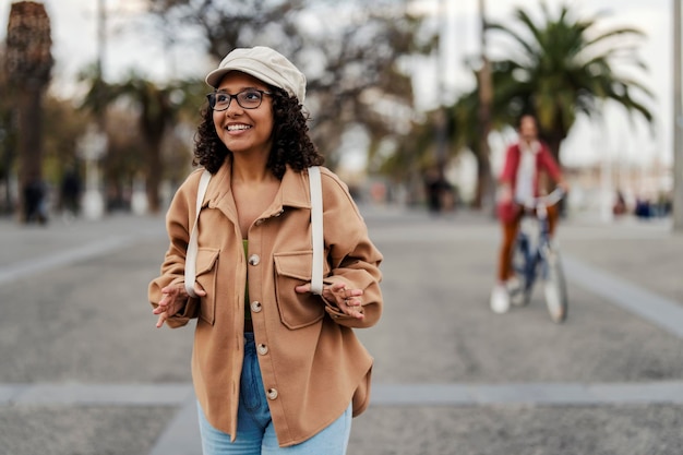 Portret van een trendy meisje met rugzak die op de stadsstraat loopt