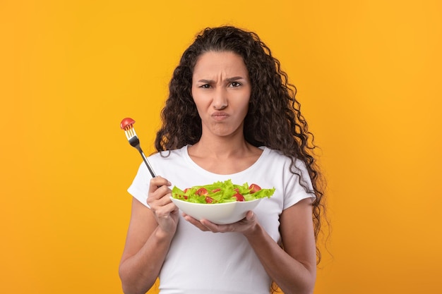 Portret van een trieste latijnse dame die een bord vasthoudt met groentesalade