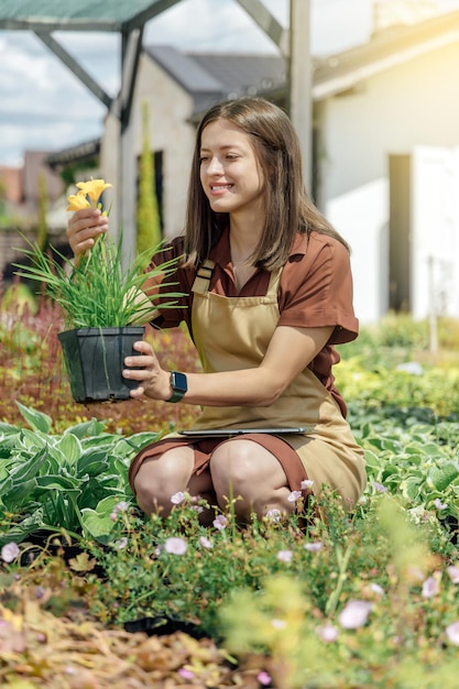 Portret van een tuinvrouw die een vaste plant in handen houdt en in de buurt van een tuinhuis werkt