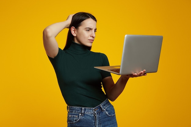 Portret van een twijfelachtig jong meisje met laptopcomputer geïsoleerd op gele achtergrond