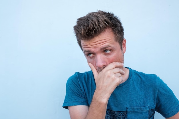 Portret van een twijfelachtige knappe man in een casual blauw shirt, kijkend met een besluiteloze uitdrukking op zijn gezicht