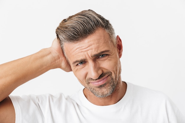 Portret van een uitgeputte man van de jaren '30 met borstelharen met een casual t-shirt dat het hoofd vastpakt vanwege pijn geïsoleerd op wit