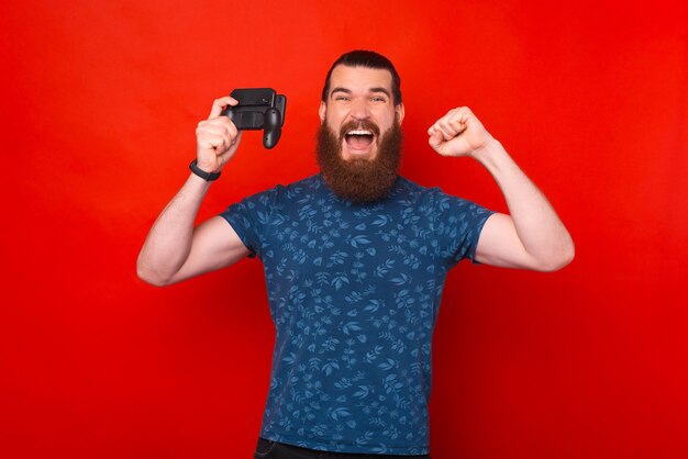 Portret van een verbaasde bebaarde hipster-man die viert en spelletjes speelt op smartphone met joystick