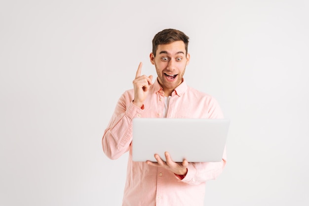 Portret van een verbaasde opgewonden jonge man die op een laptopcomputer werkt en de wijsvinger omhoog wijst met een blij gezicht op een witte geïsoleerde achtergrond. Studio shot van gelukkige mannelijke student poseren met notebook.