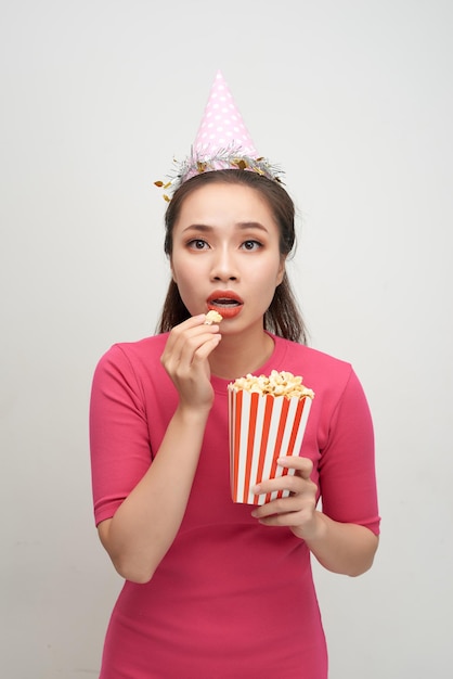 Portret van een verbaasde vrouw die popcorn houdt die over witte achtergrond wordt geïsoleerd