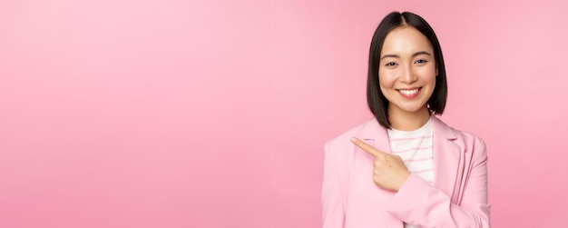 Portret van een verkoopster van een Aziatische zakenvrouw in een pak die met de vinger naar links wijst en een banneradvertentie laat zien die lacht en er professioneel roze uitziet