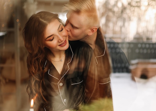 Portret van een verliefde man en vrouw die elkaar knuffelen en kussen, genomen door het raam van het huis