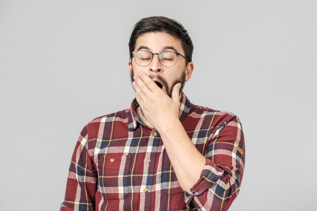 Portret van een vermoeide gapende jonge man geïsoleerd over grijze achtergrond