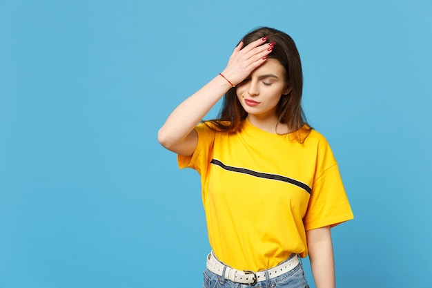 Portret van een vermoeide jonge vrouw in levendige vrijetijdskleding die de ogen gesloten houdt, de hand op het hoofd legt, het gezicht geïsoleerd op een felblauwe muurachtergrond in de studio. Mensen levensstijl concept. Bespotten kopie ruimte.