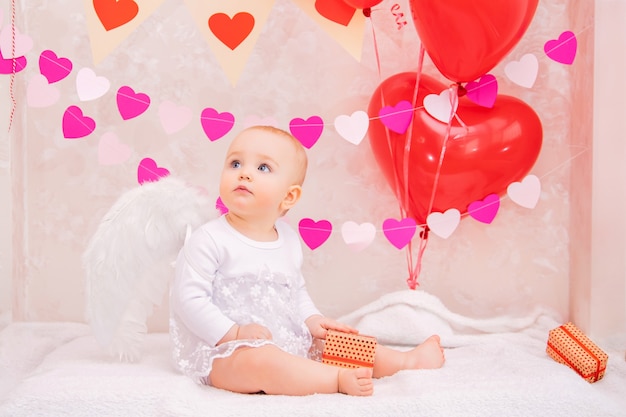 Portret van een verraste baby met witte verenvleugels, met geschenken in dozen, symbolen van Valentijnsdag.