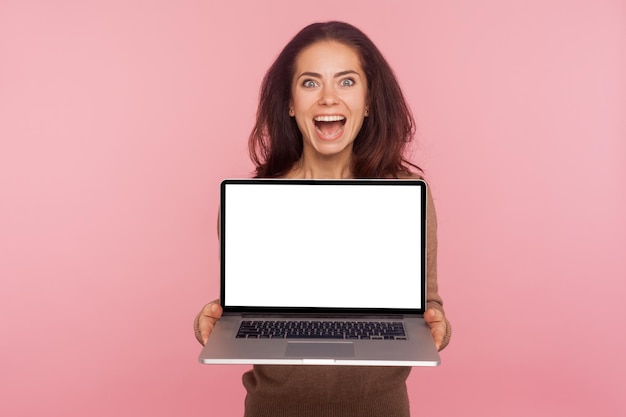 Portret van een verraste vrouw die een laptop vasthoudt met kopieerruimte op het witte scherm, een mock-up display voor internetreclame, geschokt door online service, die verbazing uitdrukt. indoor studio opname, roze achtergrond