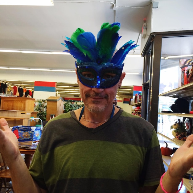 Foto portret van een volwassen man die een masker draagt en gebaren maakt terwijl hij in een winkel staat