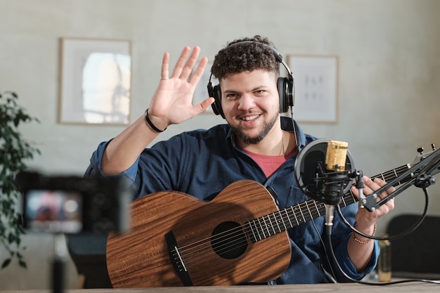 Portret van een volwassen man met een koptelefoon die naar de camera glimlacht terwijl hij met zijn handen zwaait en gitaar speelt