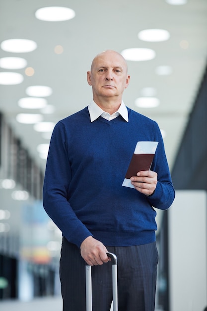 Portret van een volwassen man met kaartjes en bagage kijken terwijl je op de luchthaven staat