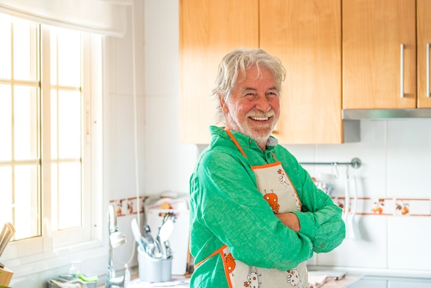 Portret van een volwassen man of senior glimlachend en kijkend naar de camera die thuis in de keuken kookt