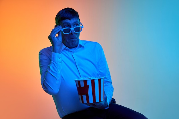 Foto portret van een volwassen man van middelbare leeftijd die zich voordeed in een d-bril en popcorn over blauw oranje met kleurovergang