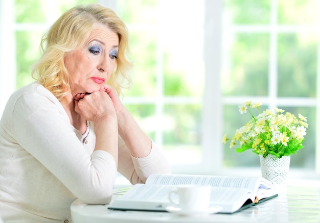 Portret van een volwassen vrouw die aan tafel zit en een boek leest