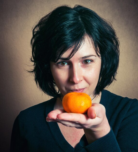 Foto portret van een volwassen vrouw die een sinaasappel vasthoudt terwijl ze tegen de muur staat