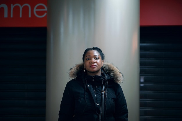 Portret van een volwassen vrouw met een kapje die tegen een zilveren zuil staat