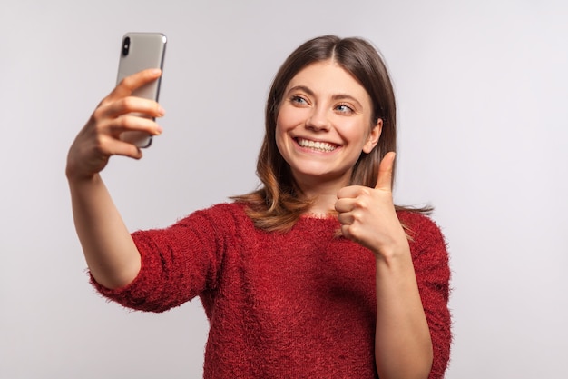 Portret van een vriendelijk meisje dat een videogesprek voert via de mobiele telefoon en duimen opsteekt, communiceert