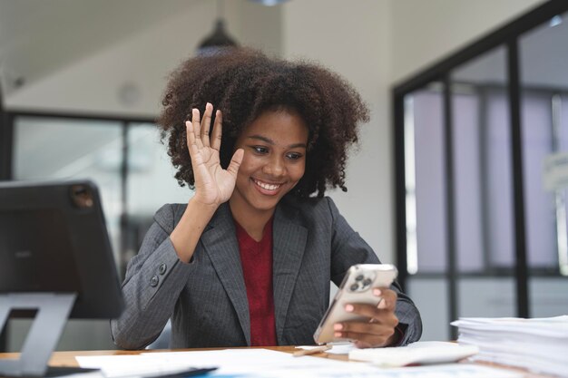 Portret van een vrij vrolijke afrikaanse vrouw die aan een bureau zit, videogesprek online via mobiele telefoon met haar cliënt