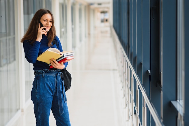 Portret van een vrij vrouwelijke student met boeken en een rugzak in de gang van de universiteit