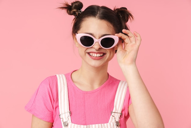 Portret van een vrolijk charmant meisje in zonnebril poseren en glimlachen geïsoleerd over roze muur