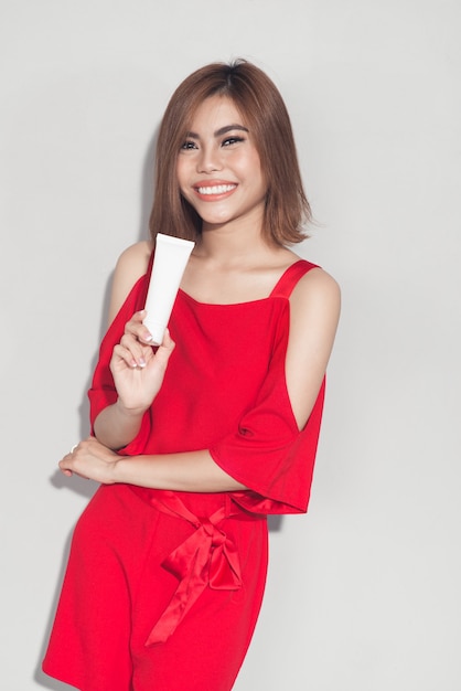 Portret van een vrolijk glimlachend modemeisje in een rode jurk met cosmetische plastic buis