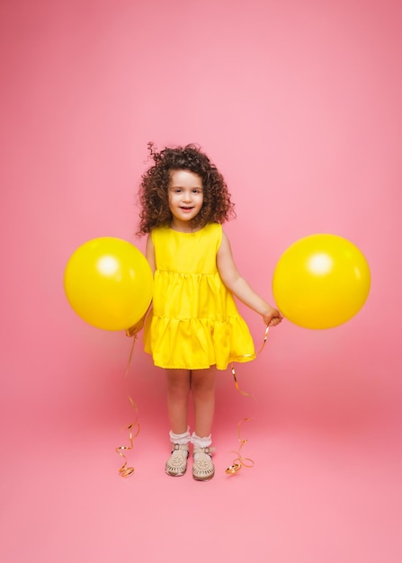 Portret van een vrolijk klein meisje geïsoleerd op een roze achtergrond met een stel kleurrijke ballonnen die poseren