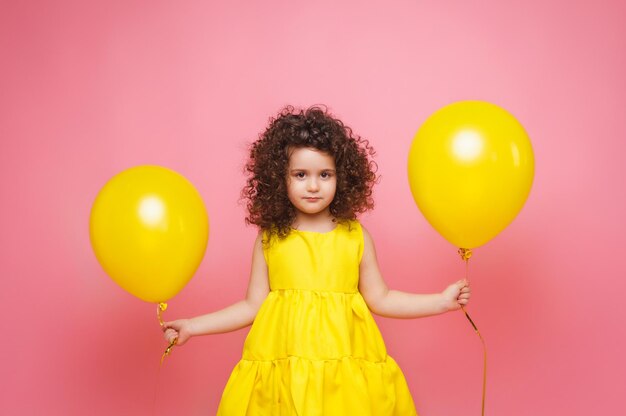 Portret van een vrolijk klein meisje geïsoleerd op een roze achtergrond met een stel kleurrijke ballonnen die poseren