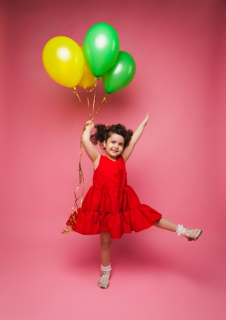 Portret van een vrolijk klein meisje geïsoleerd op een roze achtergrond met een stel kleurrijke ballonnen die poseren