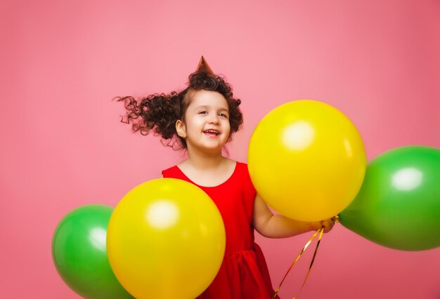 Portret van een vrolijk klein meisje geïsoleerd op een roze achtergrond met een stel kleurrijke ballonnen die poseren