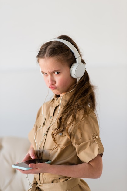 Portret van een vrolijk meisje in een stijlvolle bruine overall die naar muziek luistert op een koptelefoon