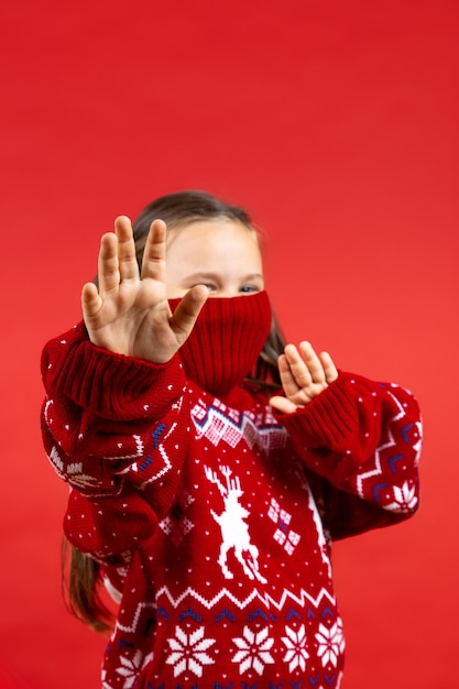 Portret van een vrolijk meisje in rode kersttrui met rendieren en met gebreide kraag op half gezicht