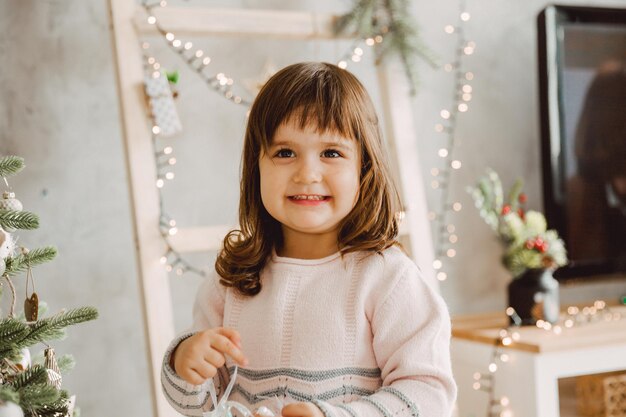 Portret van een vrolijk meisje met donker haar dat in de buurt van de kerstboom staat.