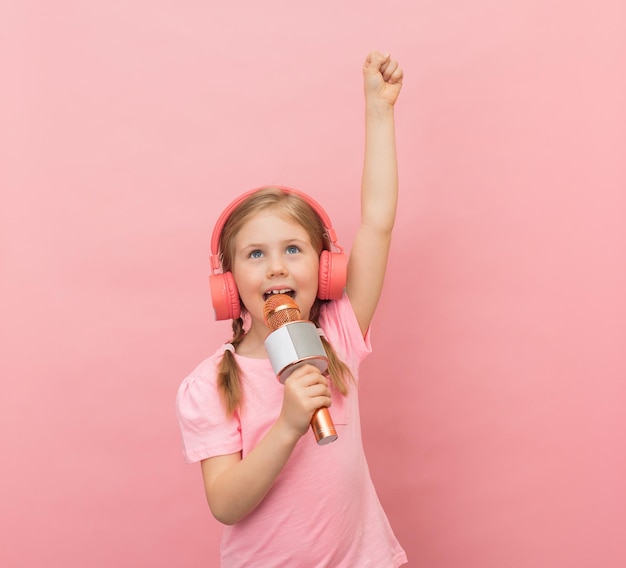 Portret van een vrolijk speels meisje dat zingt op een roze achtergrond Jonge zangeres met een microfoon