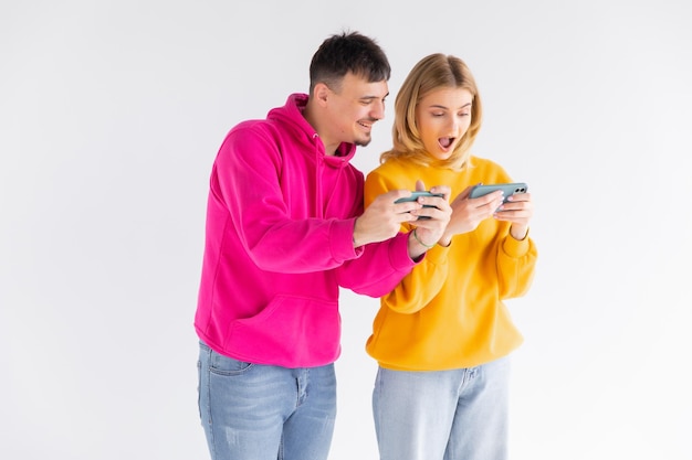 Portret van een vrolijk stel man en vrouw die samen staan tijdens het spelen van videogames op smartphones