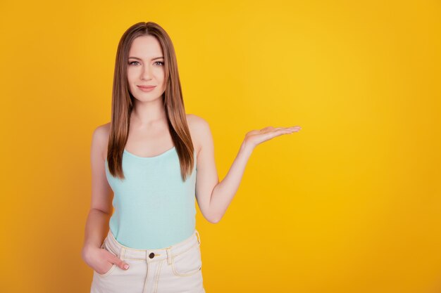 Portret van een vrolijke aardige mooie dame houdt een onzichtbare handzak op gele achtergrond vast