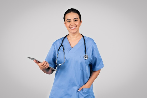 Portret van een vrolijke arts-Latijns-dame in blauw uniform met klembord en glimlachend in de camera