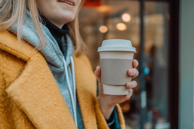 Portret van een vrolijke blanke vrouw die lacht en koffie drinkt terwijl ze door de stad loopt