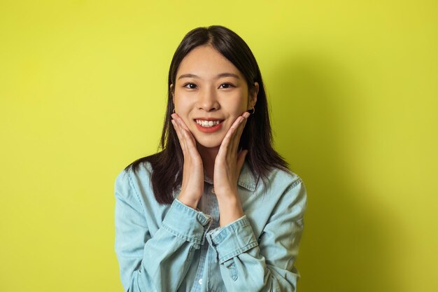 Portret van een vrolijke Japanse vrouw die haar gezicht over gele achtergrond aanraakt