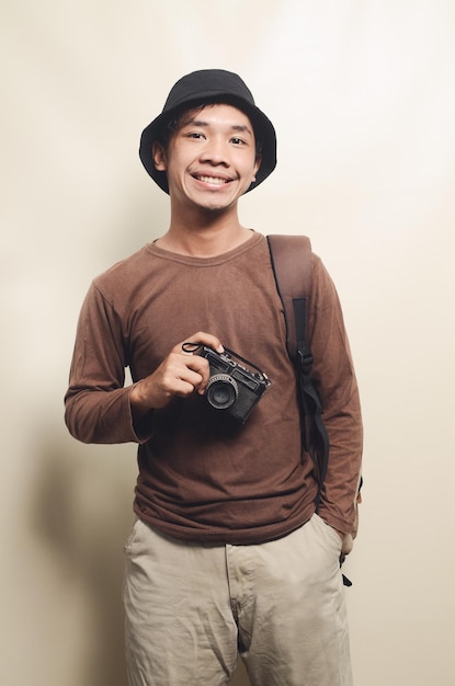 Portret van een vrolijke jonge Aziatische man met een zwarte hoed met camera en rugzak geïsoleerd op de achtergrond